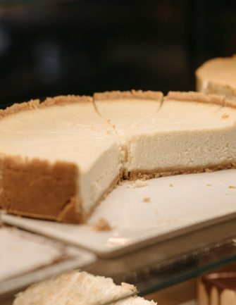 Close-up of assorted cheesecakes on a glass shelf, showcasing their creamy texture.