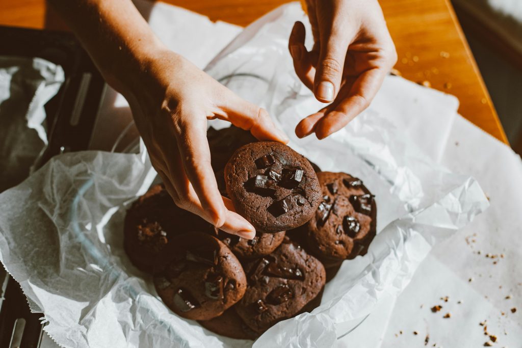 A person holding freshly baked chocolate cookies, perfect for dessert and snack imagery.
