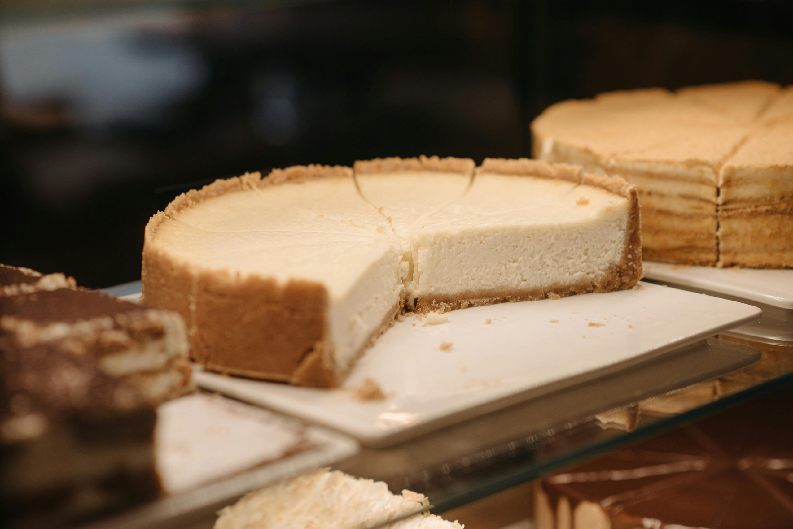 Close-up of assorted cheesecakes on a glass shelf, showcasing their creamy texture.